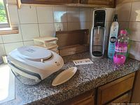 Grill, glass containers, carbonator, bottles and box of cylinders on countertop
