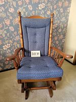Front view of blue upholstered wood glider rocking chair showing seat, back cushion, arms, and glider base