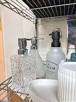 clear glass and frosted dispensers with chrome pumps alongside white ceramic dishes on shelf