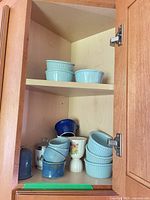 Cabinet showing stacks of light-blue ramekins on upper shelf, assorted blue ceramics, floral egg cups and canisters on lower shelf