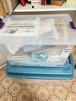 Two lidded storage bins with visible packaged mattress protector and linens inside