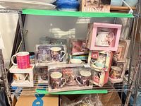 Shelf view showing multiple boxed mug sets, travel mug box and individual mugs