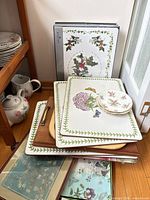 Stacked laminated placemats with floral hydrangea motif, wooden boards beneath, small floral saucers on top