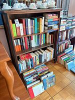 Front view of bookcase filled with books, teacups and saucers displayed on top