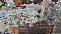 Group shot of porcelain cake stands, candlesticks, bud vases, glass bowl and butter dish on shelf