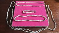 Full view of necklace, bracelet and strand laid on pink surface