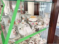 Multiple porcelain pieces on glass shelf showing overall lot