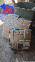 Two damaged, strapped cardboard boxes containing patio table and umbrella base