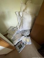 Stack of white pillows, folded blue floral quilt, gray floral bedding, sealed sheet sets