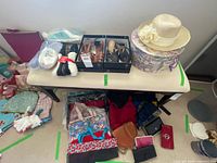 Overview of table showing shoes in open boxes, packaged slippers, straw hat on floral hat box, assorted bags and wallets on floor