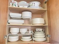 Dinnerware stacked in cupboard showing variety of plates, bowls, casserole dishes and teacups