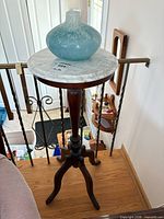Full view of pedestal side table showing marble top, wooden base and tripod legs