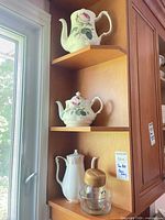 Three-shelf view showing two floral teapots, ceramic creamer, glass jar with wood lid and glass bowl