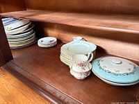 Stacked dinner plates, side plates, two serving dish lids visible on cabinet shelf