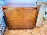 Front view of medium brown two-drawer wood veneer file cabinet with integrated handles and lock
