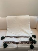 Full view of cream blanket draped on sofa showing size and tassel detailing