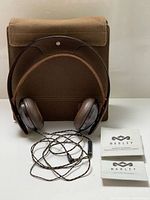 Headphones coiled with braided cable, fabric case behind, manuals at right