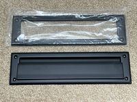 Both pieces of the matte black mail slot, still partly in plastic wrap