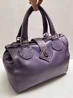 Front and side view of lavender handbag held by handle