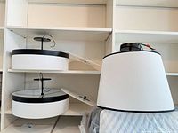 Two disassembled plastic-diffuser drum lights and one fabric-shade drum light on shelving
