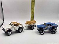 White pickup towing trailer with gold boat alongside blue off-road car; ruler shows scale
