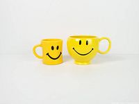 Front view of both yellow smiley face mugs