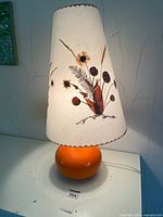 Full view of lamp showing orange base and pressed flower shade
