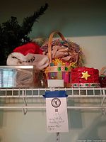 Shelf with artificial tree sections, Santa hat, clear box of ornaments, multicolour wood basket, red woven basket