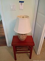 Lamp with shade on red wood side table, full view