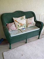Front view of green wicker loveseat with seat cushion and three throw pillows