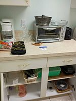 Lot overview showing coffee maker, toaster oven, cookbooks, towel, cutting board, plastic bins