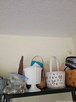 Shelf view showing white plastic strawberry basket, natural wood-strip square basket, small brown wicker basket, white pedestal not part of lot