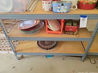 Front view of shelving unit loaded with dishes, shows three particle board shelves and gray metal frame