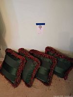 Three of the four green satin pillows with red multicolour fringe shown leaning against wall
