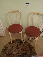 Two cream metal bistro chairs with brown vinyl seats placed on small round patterned rug