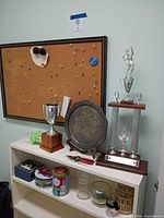 Front view of bookcase showing trophies, metal plate, pliers, tins, glass jars, planters
