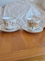 Two Royal Stafford teacups on saucers showing gold floral decoration and ribbed bodies