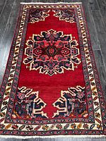 Full view of entire rug showing red field, central medallion, borders and fringe