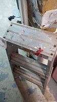 Full view of folded aluminum ladder showing three steps and top platform
