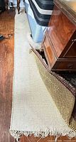 Flat-weave natural fiber area rug laid on hardwood floor, fringe visible, partially covered by patterned mat