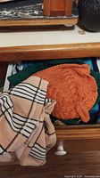 Drawer contents showing orange knit tea cosy, striped dish towel, part of green fabric pad