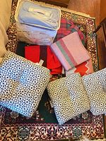 Group of bed skirt, throws, blankets, afghan and three cushions displayed on rug