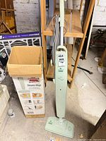 Full view of steam mop standing next to box