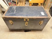 Front and top view of steamer trunk showing brass latches, lock, black paper covering and wear