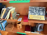 Books on shelf with ship bookend, staples, wooden mug, metal bookends