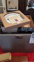 Grey metal storage box with cardboard boxed collector plate and COA leaflet visible