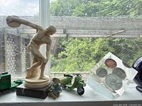 Windowsill view showing discus thrower figurine, green truck, cowboy, scooter, coin cube