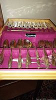 Flatware set arranged in case showing spoons, forks and Tradition plaque