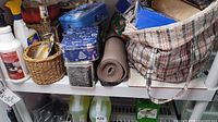 Shelf with cleaners, wicker basket containing stemware, tins, tote bag, rolled mat, Zep cleaner jugs underneath