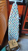 Full-size ironing board standing upright with patterned cover visible